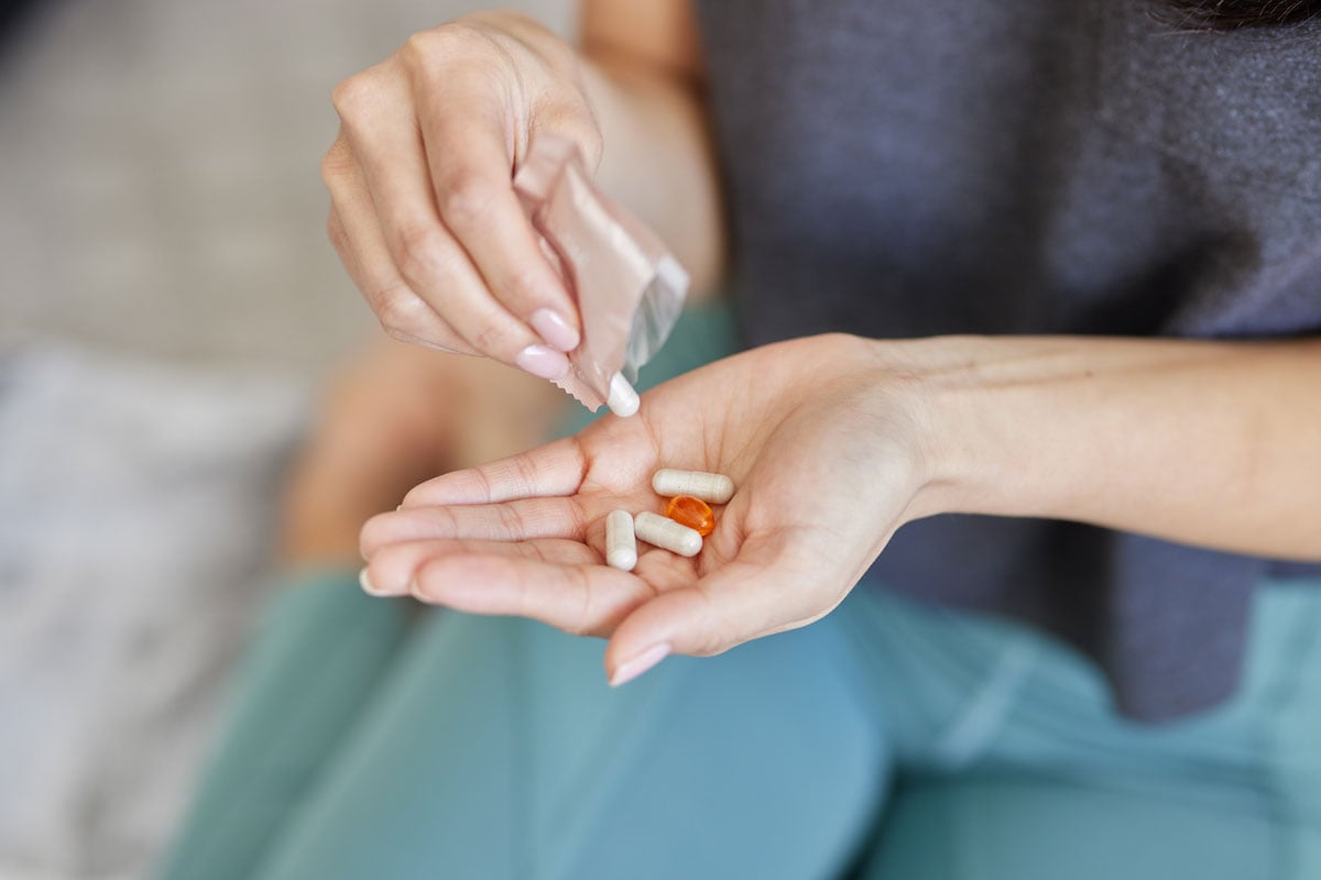 Woman holding Vitalité multivitamin capsules and omega softgel from daily wellness packet.