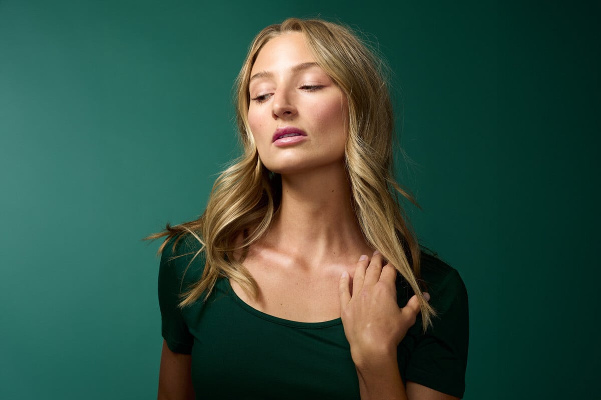 A beautiful woman in a green room with glowing skin and golden complexion