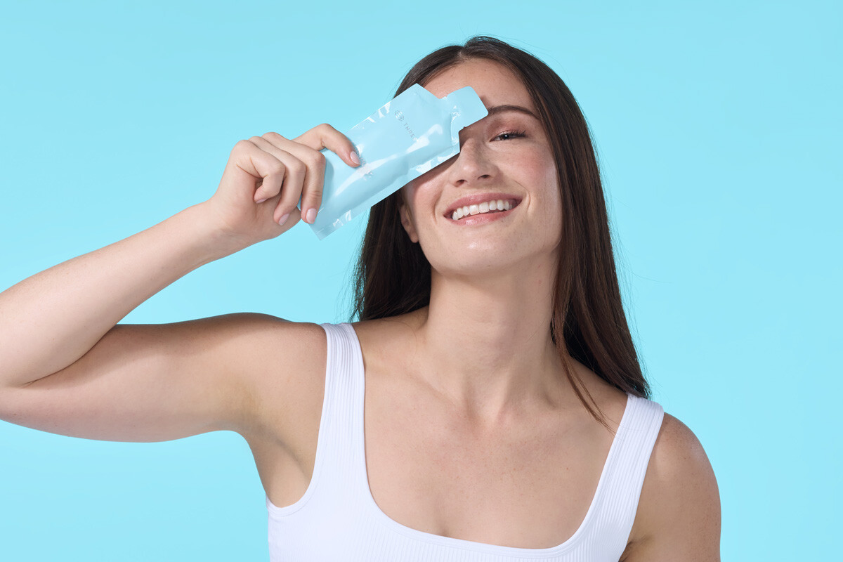 a woman holding a pouch of Collagène by THREE collagen supplement up to her face showing her radiant skin and complexion