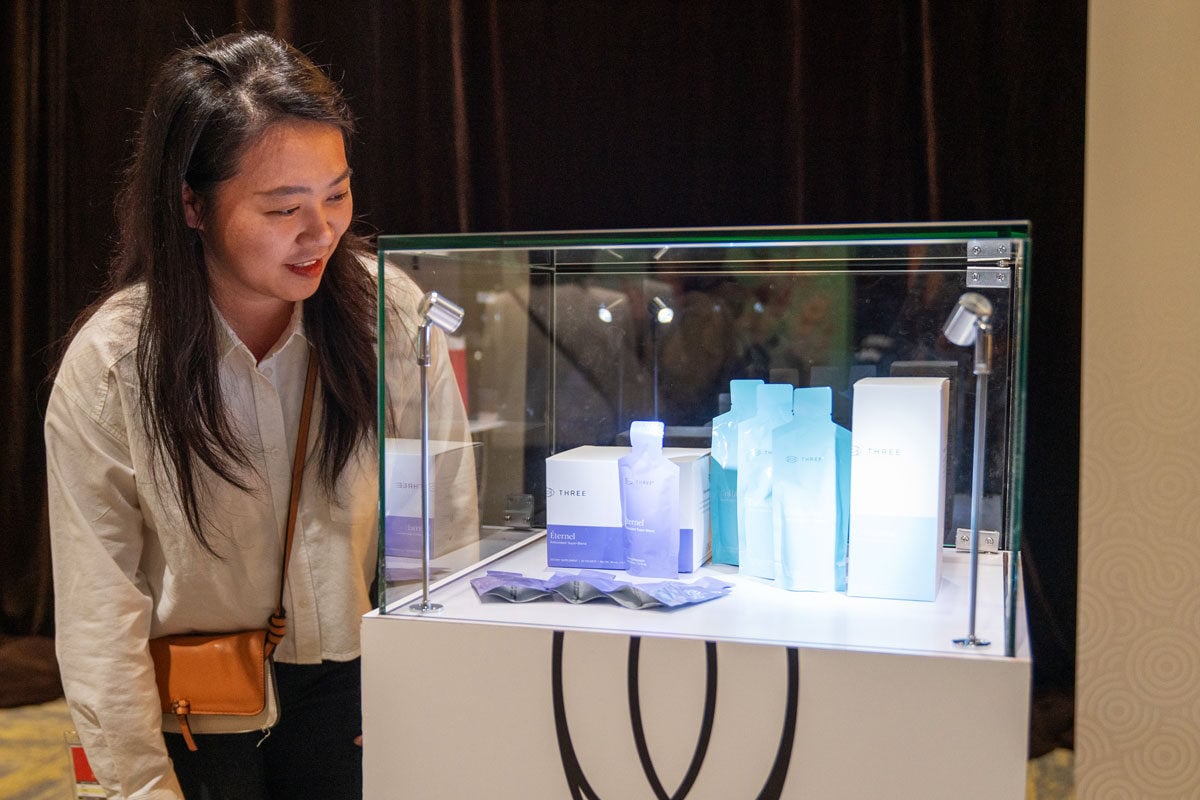 a woman standing next to a glass case of Éternel and Collagène by THREE International