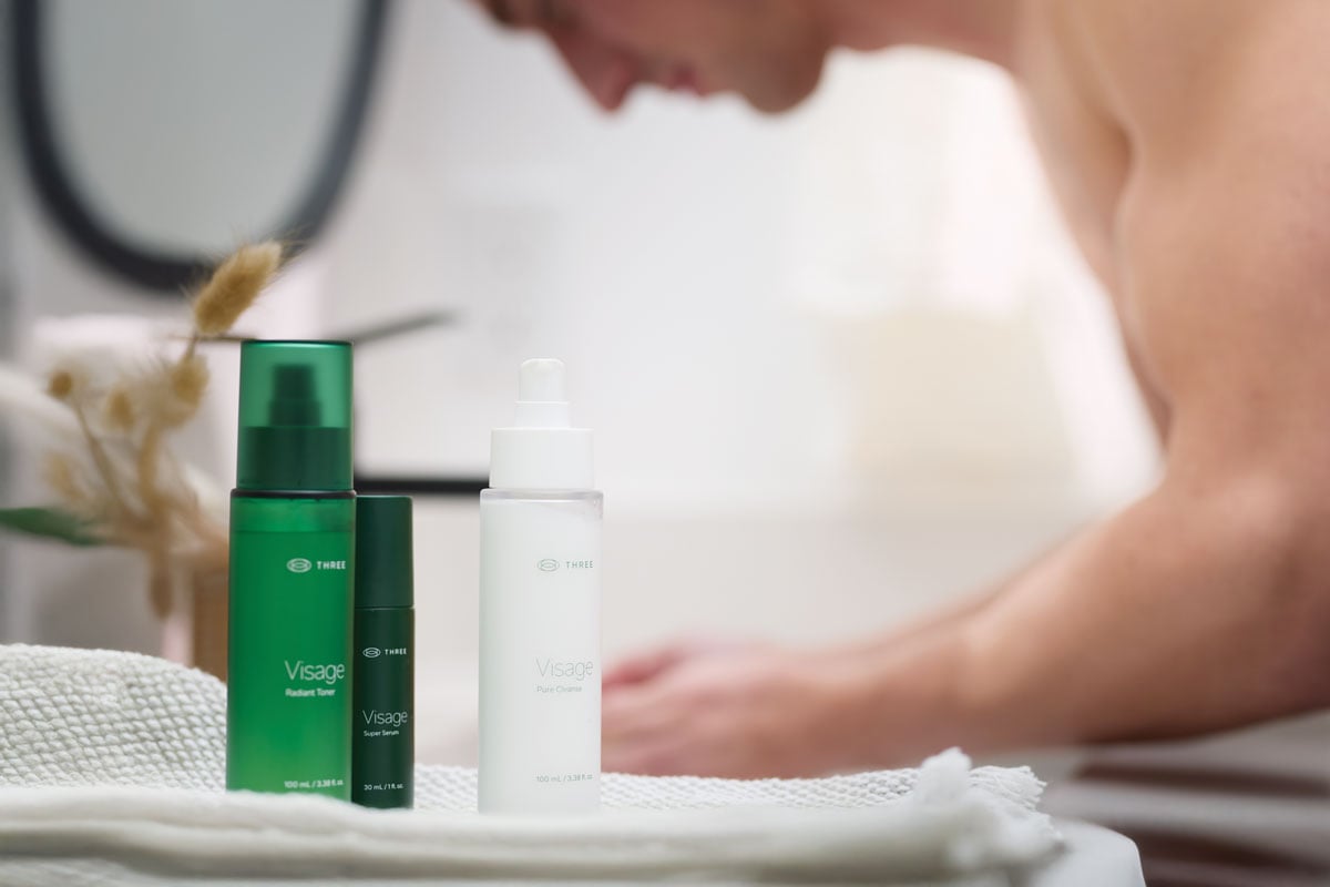 a man in the background with the Visage Skincare Collection by THREE in the foreground