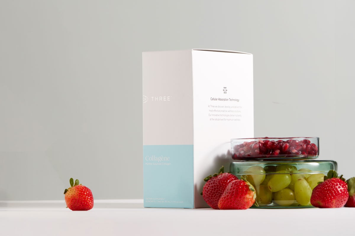 A package of Collagène by THREE International sitting next to strawberries grapes and pomegranate