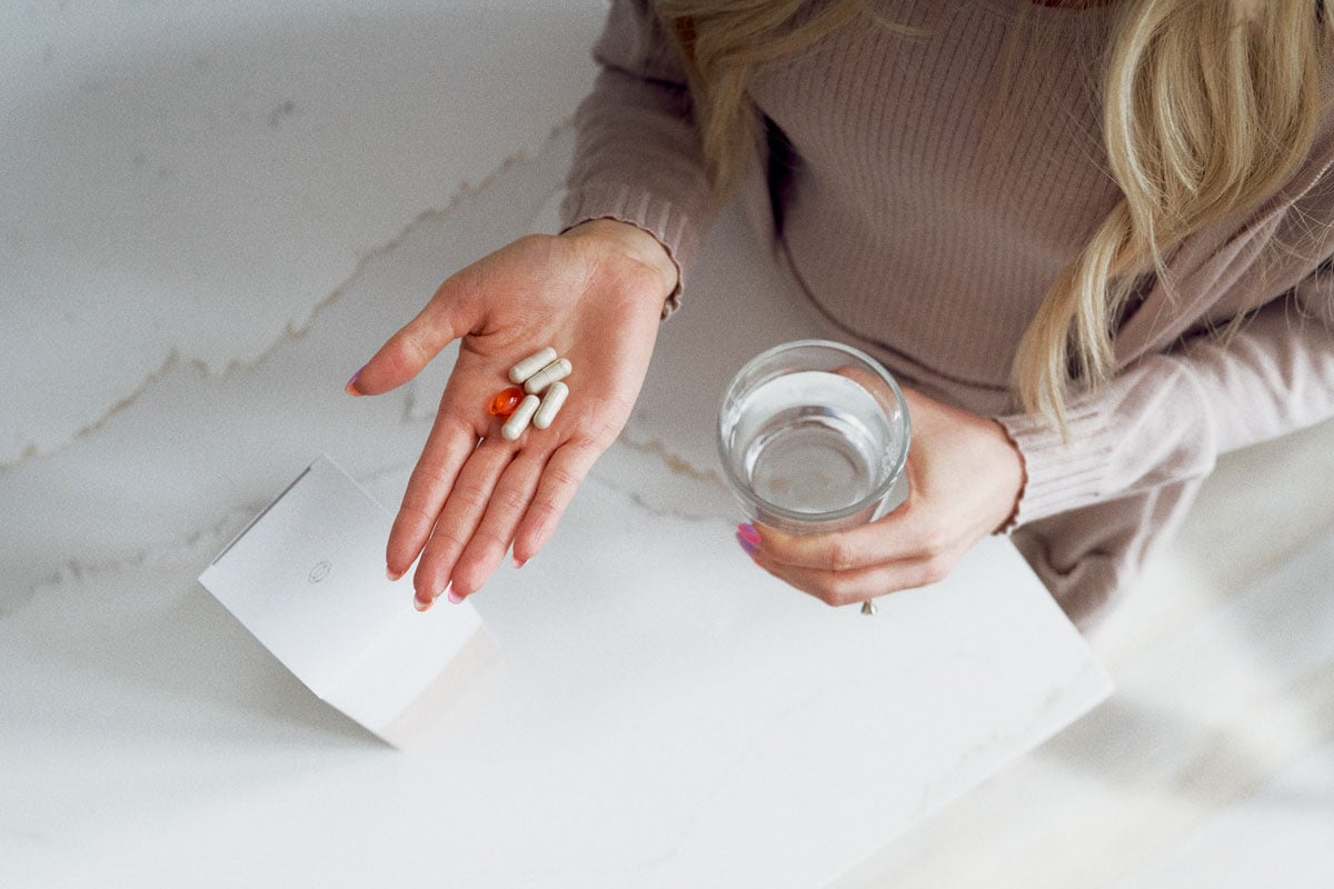 woman in her kitchen taking her daily Vitalité by THREE supplement