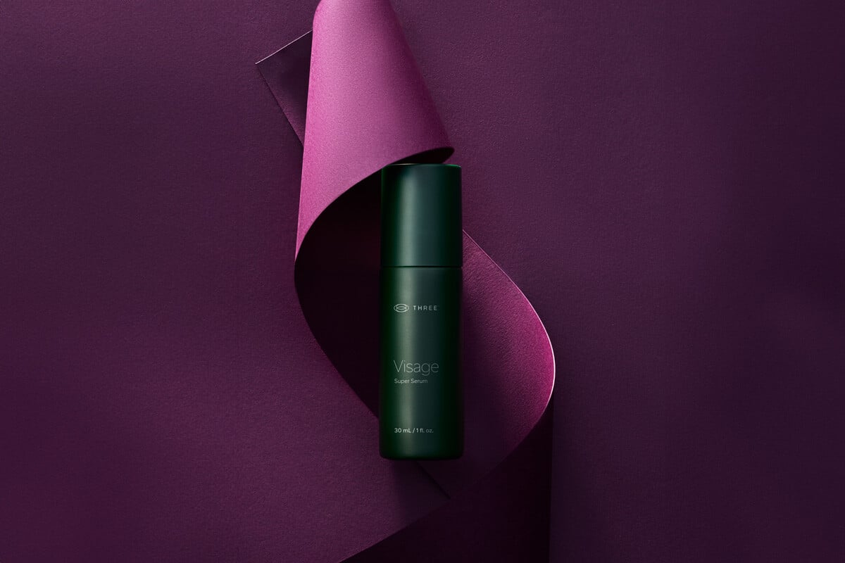 A bottle of Visage Super Serum by THREE in elegant purple backdrop