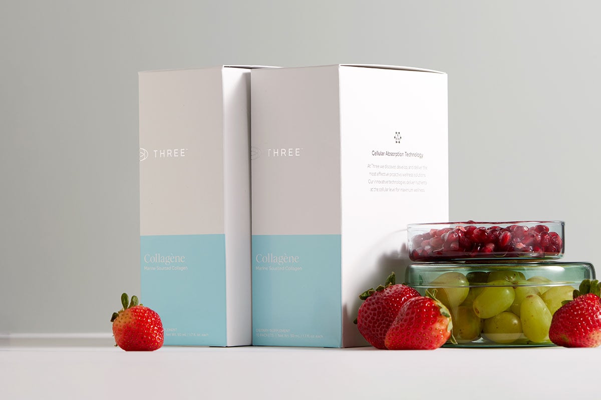Collagéne by THREE supplements sitting next to fresh strawberries pomegranates and grapes