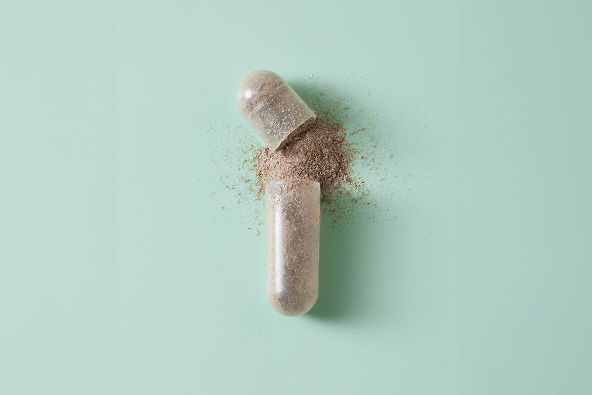 an open capsule of Vitalité by THREE supplement on a green background